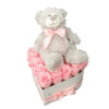 siv plišasti medvedek z roza pentljo sedi na roza rožah v sivi srčkasti škatli