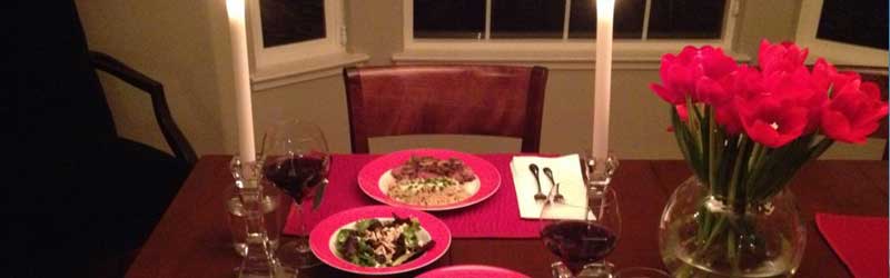 Valentine's dinner table with pink flowers, plates and two candles